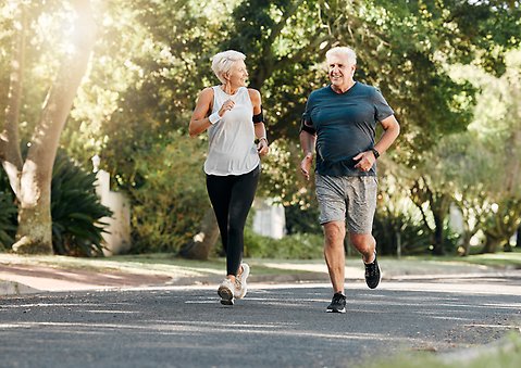 Två seniorer, en kvinna och en man, är ute och joggar.