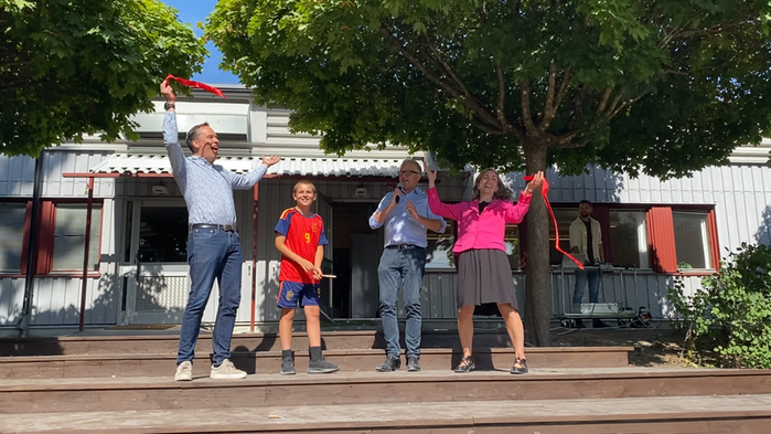 En pojke klipper av ett rött band vid invigning av Breddenskolans nya lekytor.