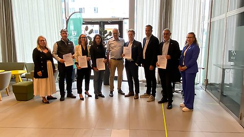 En grupp personer, män och kvinnor står uppradade bredvid varandra med dokument i händerna. 