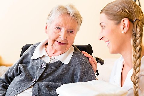 En äldre kvinna sittandes i en rullstol och en yngre kvinna lägger handen på kvinnans axel.